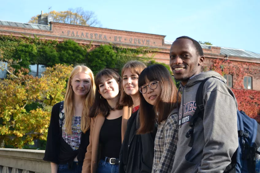 A group of international students posing in front of an autumnal Palaestra